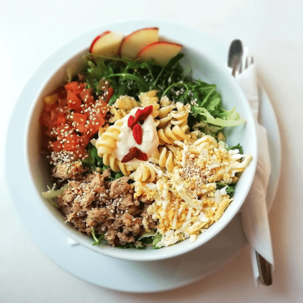 Colorful healthy bowl with fresh ingredients including apple slices, greens, grains, and various toppings